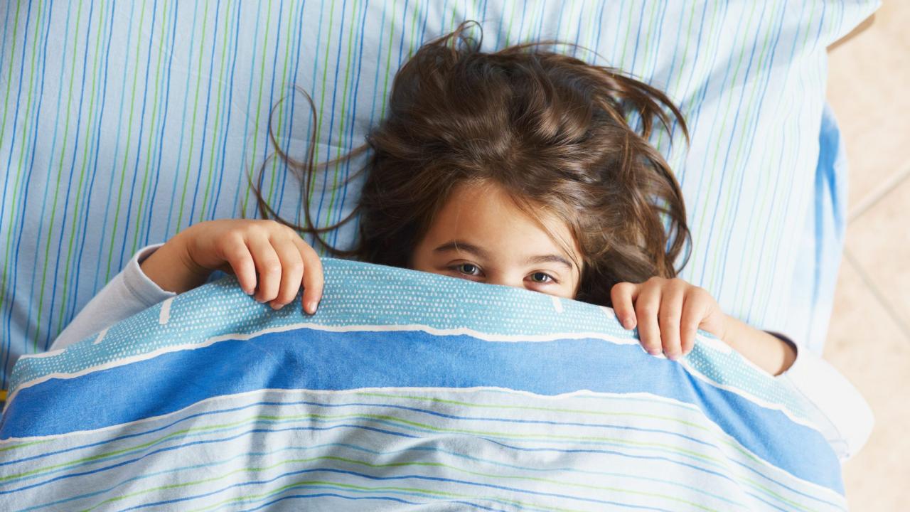 Girl under covers, looking at camera.