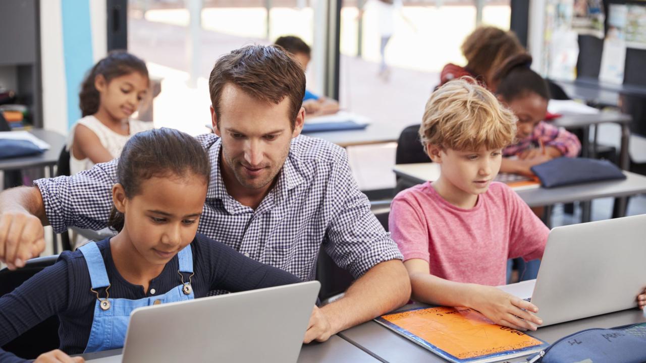 Teacher helping young students using laptops in class