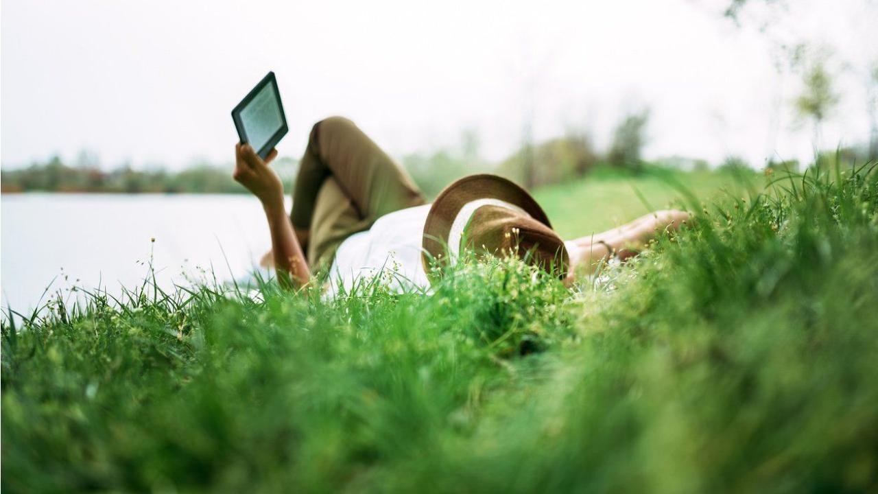 laying-in-grass-reading-a-book-on-an-ereader