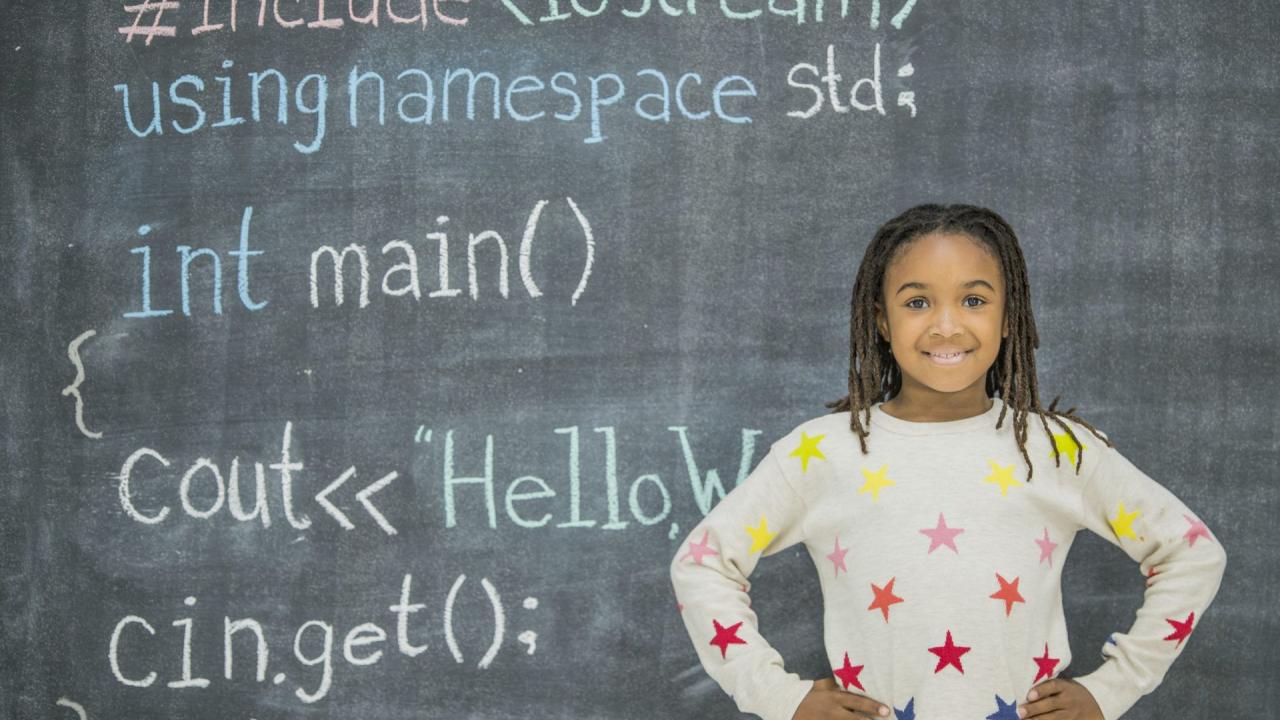 Girl standing in front of a chalkboard with code written on it