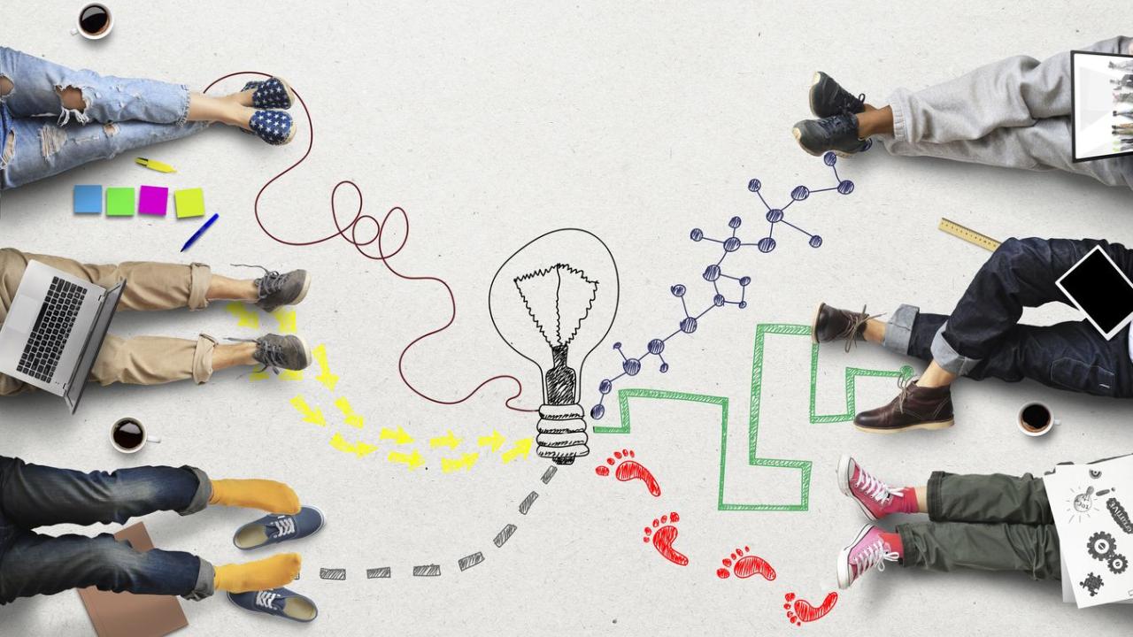 Students sitting on the ground with different colored pathways tracing their way to a lightbulb in the center