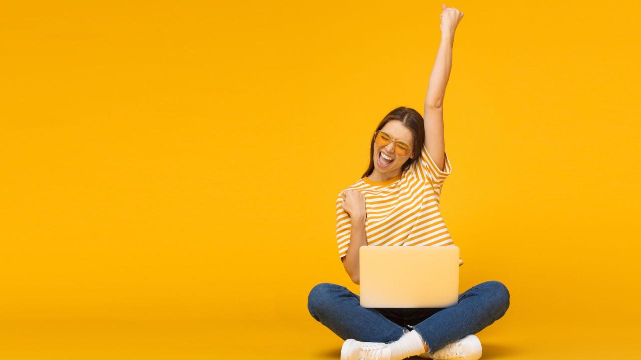happy student cheering next to laptop against yellow background