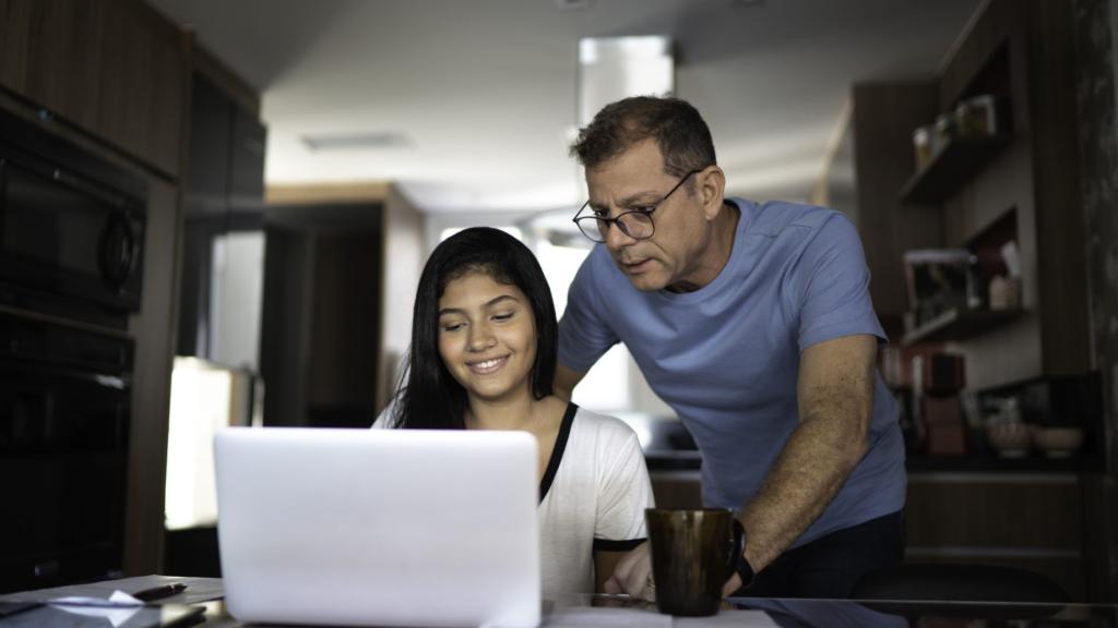father helping daughter with homework on her laptop