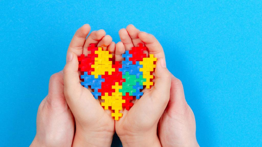 Adult and kid hands holding colorful heart on blue background. World autism awareness day concept.