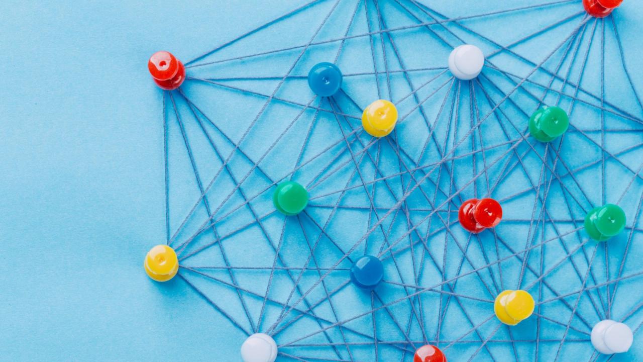 Small network of pins (Thumbtack)and string, An arrangement of colorful pins linked together with string on a pale blue background suggesting a network of connections.