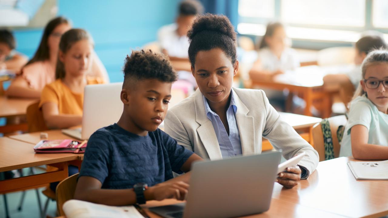 African American teacher and her student using laptop during computer class at elementary school.