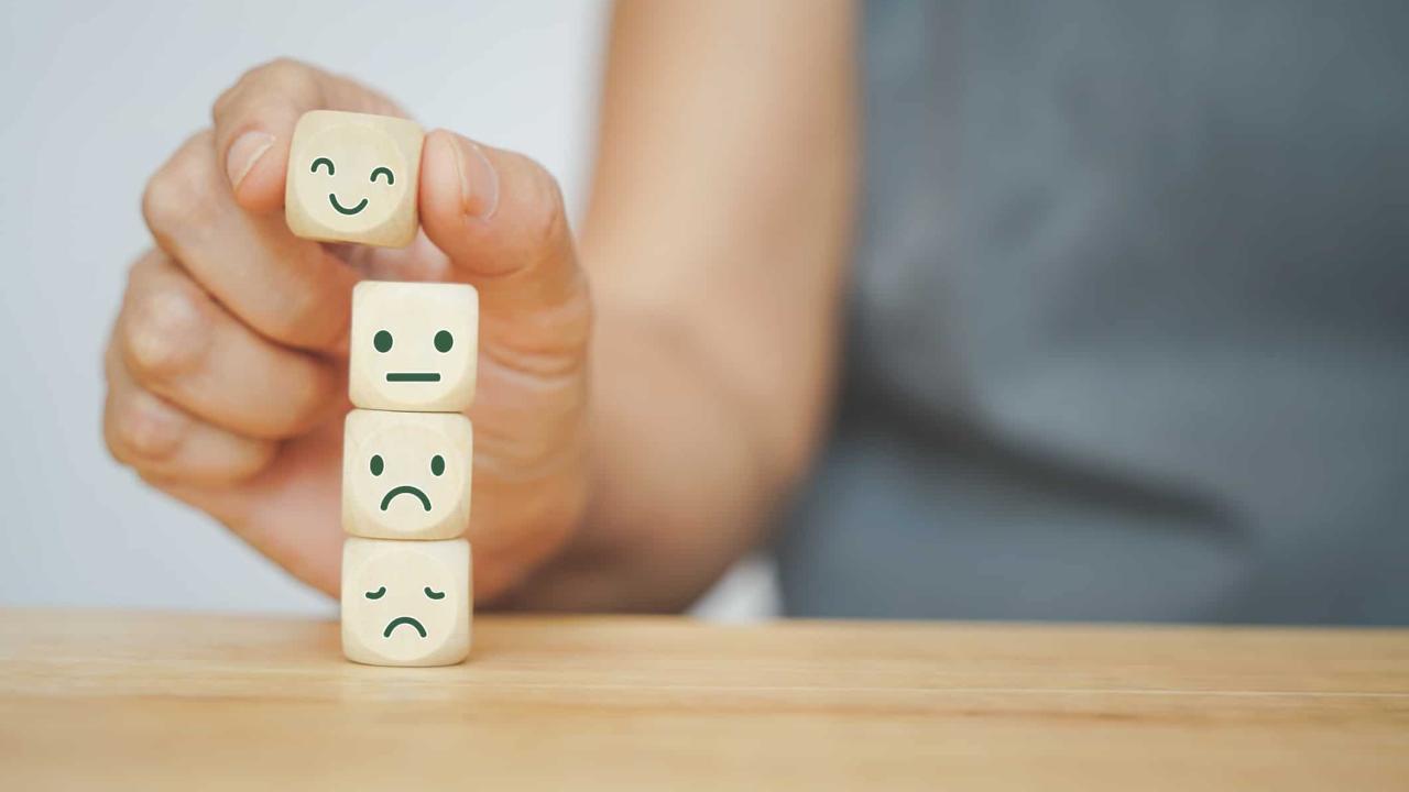 senior human hand selected happy face wood cube and others on green background for customer service evaluation, feedback, satisfaction survey or mental heath concept
