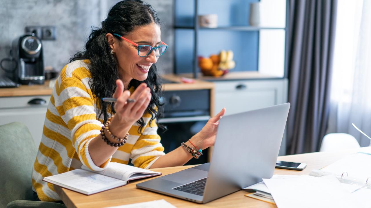 Middle aged woman working from home, while in quarantine isolation during the Covid-19 health crisis. Portrait middle aged  woman smiling and looking at laptop screen