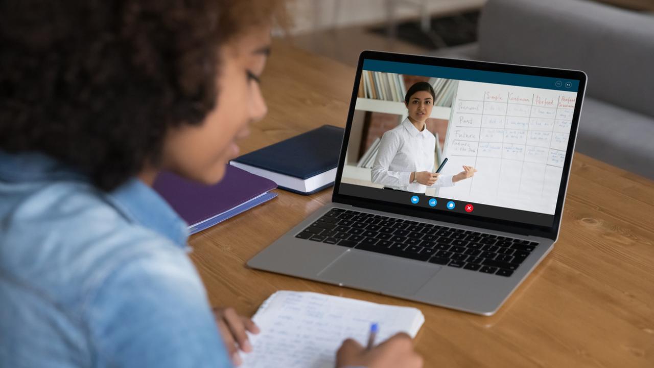 African teenager girl studying online seated at desk with laptop