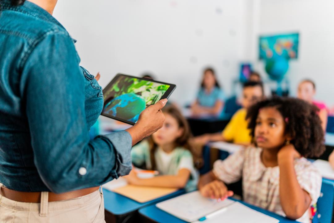 Mid adult teacher talking and using digital tablet during environment class at school