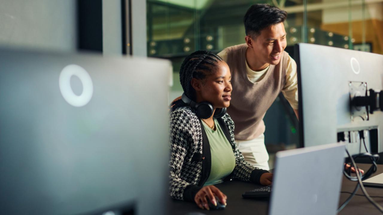 Software engineers collaborating on a project, analyzing code on computer monitors in office