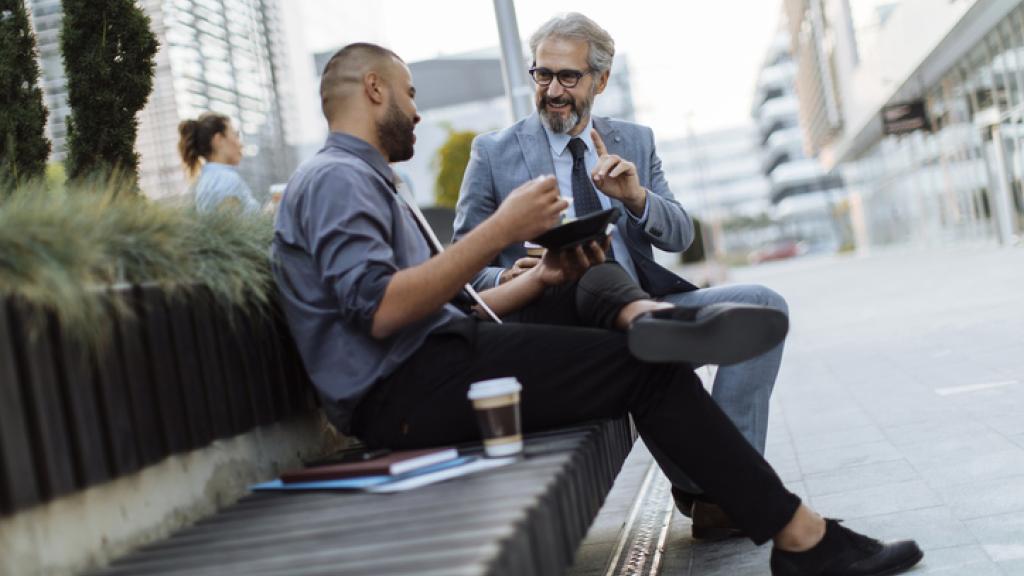 Two coworkers discussing work over lunch outside their office building while on a break