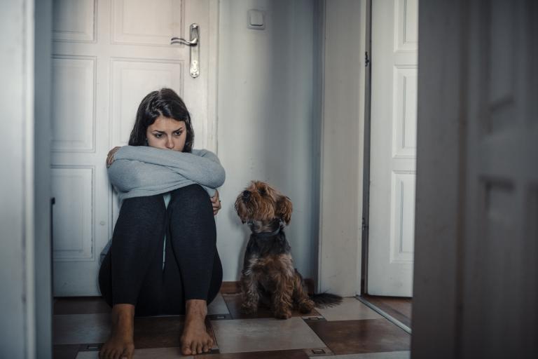 Woman With A Mental Problems Is Sitting Exhausted On The Floor With Her Dog Next To Her
