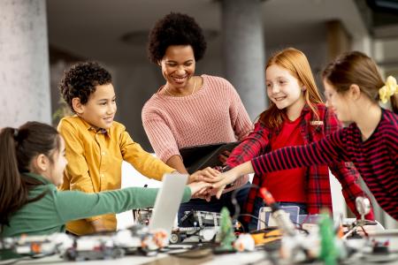 Happy kids with their African American female science teacher with laptop programming electric toys and robots at robotics classroom