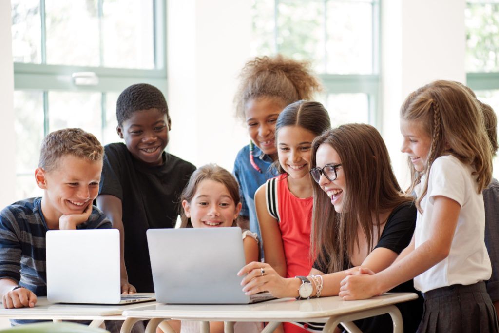 School children using laptop with teacher in the classroom