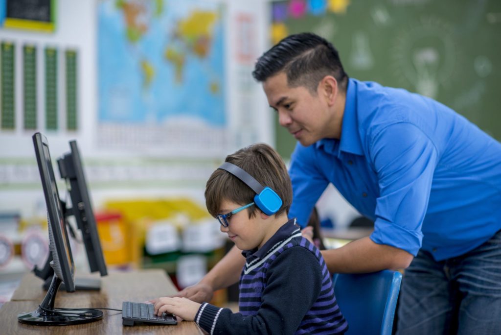 Male teacher helping student on computer