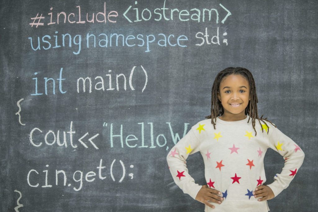 Girl standing in front of a chalkboard with code written on it