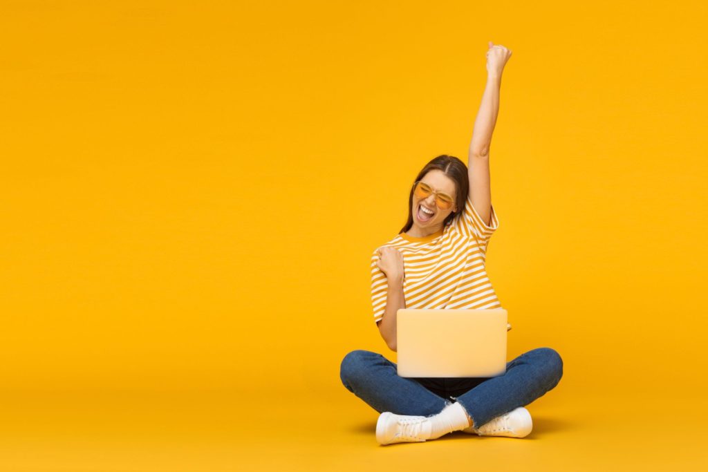happy student cheering next to laptop against yellow background
