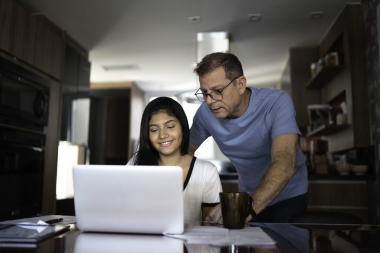 father helping daughter with homework on her laptop