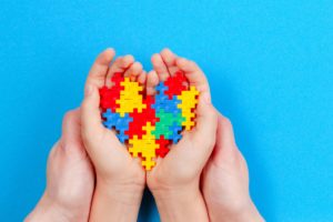 Adult and kid hands holding colorful heart on blue background. World autism awareness day concept.