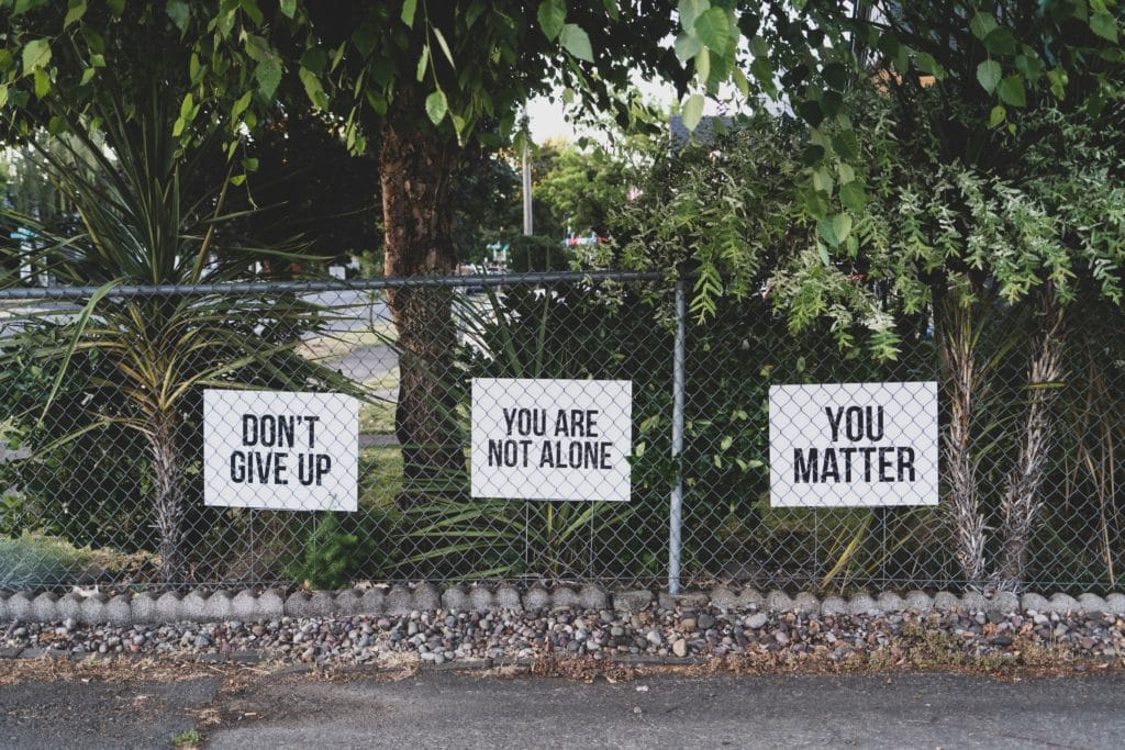 Three signs on a metal fence read: Don't give up, You are not alone. You matter. The image is specific to this post and aimed to comfort those who are affected by cyberbullying.