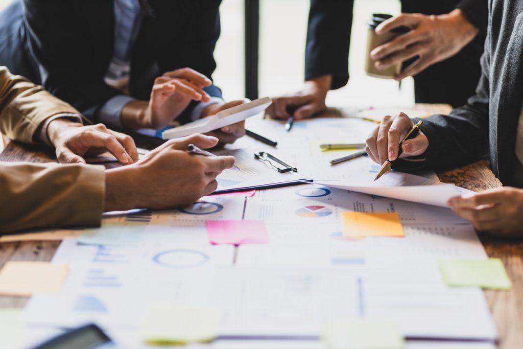People working together over table of papers and sticky notes, only their hands are visible.
